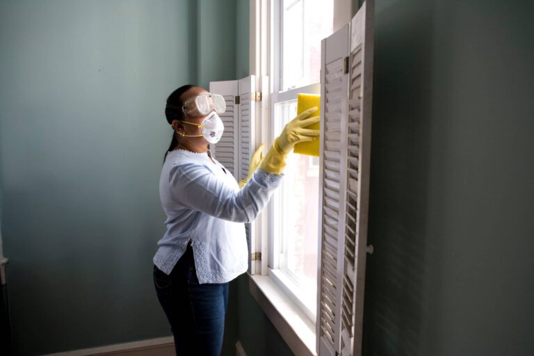 A woman cleaning windows wearing mask and goggles